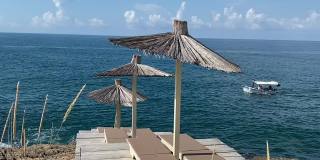 夏季地中海岩石海岸风景优美的海滩。稻草伞和舒适的阳光躺椅。船在海上航行。田园诗般的夏天海景。