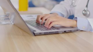 医生的双手在电脑上打字，医生在医务室用听诊器工作，医生的双手在键盘上打字记录患者在医院的病史视频素材模板下载