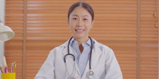 摄像头查看亚洲女医生微笑会与患者在线咨询健康健康生活，智能医生穿着白大褂，带着听诊器视频通话在医院