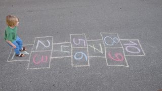 沥青上画着小男孩的腿和跳房子。春天，孩子们在操场上玩跳房子游戏。儿童户外活动。视频素材模板下载