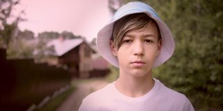一个带着帽子的严肃悲伤的男孩在村子外面看着相机，电影拍摄