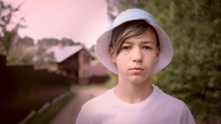 一个带着帽子的严肃悲伤的男孩在村子外面看着相机，电影拍摄视频素材模板下载