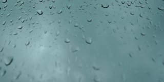 抽象的自然模式的雨滴孤立在多云的背景。在潮湿的汽车玻璃表面随机滑动。窗外阴天下雨。有选择性的重点