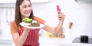年轻女子在手机上展示盘子里的牛排。年轻女子用手机展示关于食物健康的视频博客。制作牛排的照片和视频。