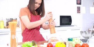 年轻女子研磨胡椒，在炉子上用一个大的胡椒研磨机把胡椒磨成盘子，用来煮肉或蔬菜。年轻的妇女们在厨房里帮忙切蔬菜。