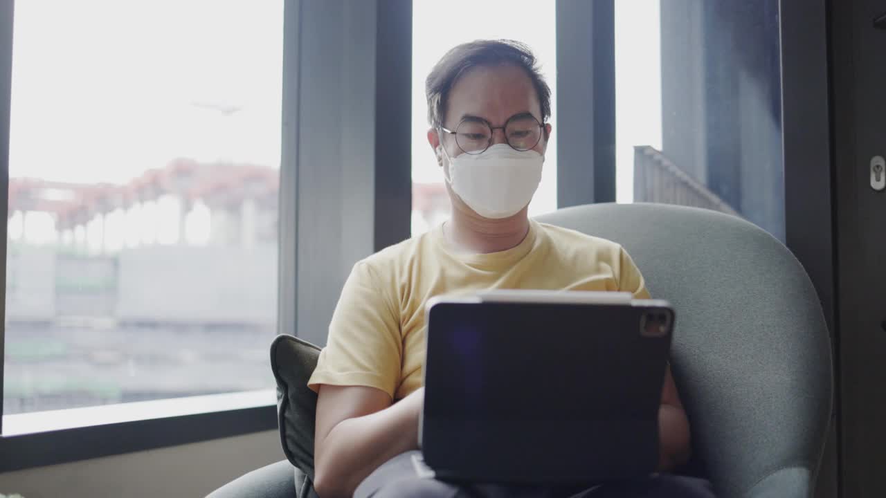 亚洲中年男子戴着眼镜，面罩，在办公空间使用笔记本电脑前喷酒精洗手。预防灰尘和COVID-19。与人保持社交距离。免费的网络