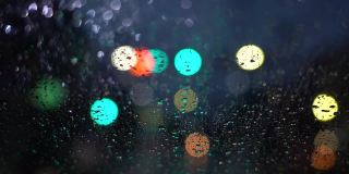 在雨夜开车。从车流中聚集的模糊光线，雨水打在前镜上。视频缓慢的运动。