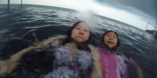 亚洲母亲和女儿放松在游泳池在他们的假期在酒店与家人，生活方式的概念。