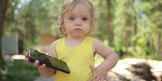 小有趣可爱的金发女孩，孩子，蹒跚学步的孩子，在夏天的乡下玩大黑色智能手机。健康快乐的童年理念。孩子和技术。