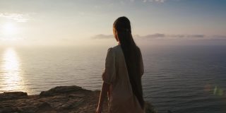 童话故事里的长发小女孩清晨走到悬崖边，欣赏美丽的海景。女孩性格会日出在高山附近的海。仙境景观视图