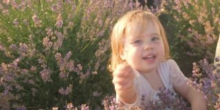 一个漂亮的女孩拿出一朵花。日落时一片紫色的淡紫色幸福，微笑，热爱自然。孩子在户外，家人在一起。慢镜头，特写。