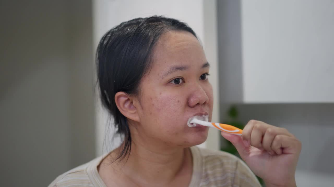 亚洲女人在浴室里刷牙，镜子里映出她的牙齿