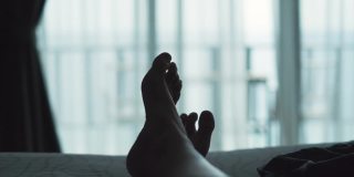 一个放松的女人躺在床上，交叉腿在毛毯上，在酒店度假胜地看风景
