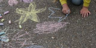 儿童户外油漆。小女孩在柏油路上用彩色粉笔画画。儿童创造性发展