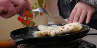 用来煎生面团做薄饼的大煎锅。Maslenitsa节日，斯拉夫人春季聚会的重要庆祝活动，街头美食节。一个男人用叉子把煎饼从煎锅里拿出来