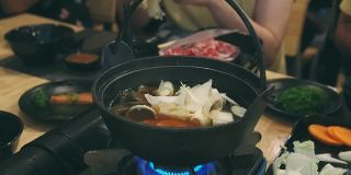 这名女子在一家日本餐馆里把金蘑菇放进涮锅里。和家人共进晚餐。