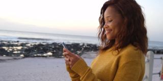 微笑的非裔美国女性在海滩上使用智能手机