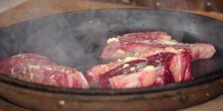 在铁锅里煎牛排。这家餐厅的专业厨师在家做饭。厨师把一块肉放在火上烤。煎烟。生肉蒸煮过程。