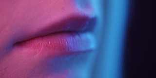 女性嘴唇在霓虹灯特写。这个女人在彩色的光中性感地张开了嘴。