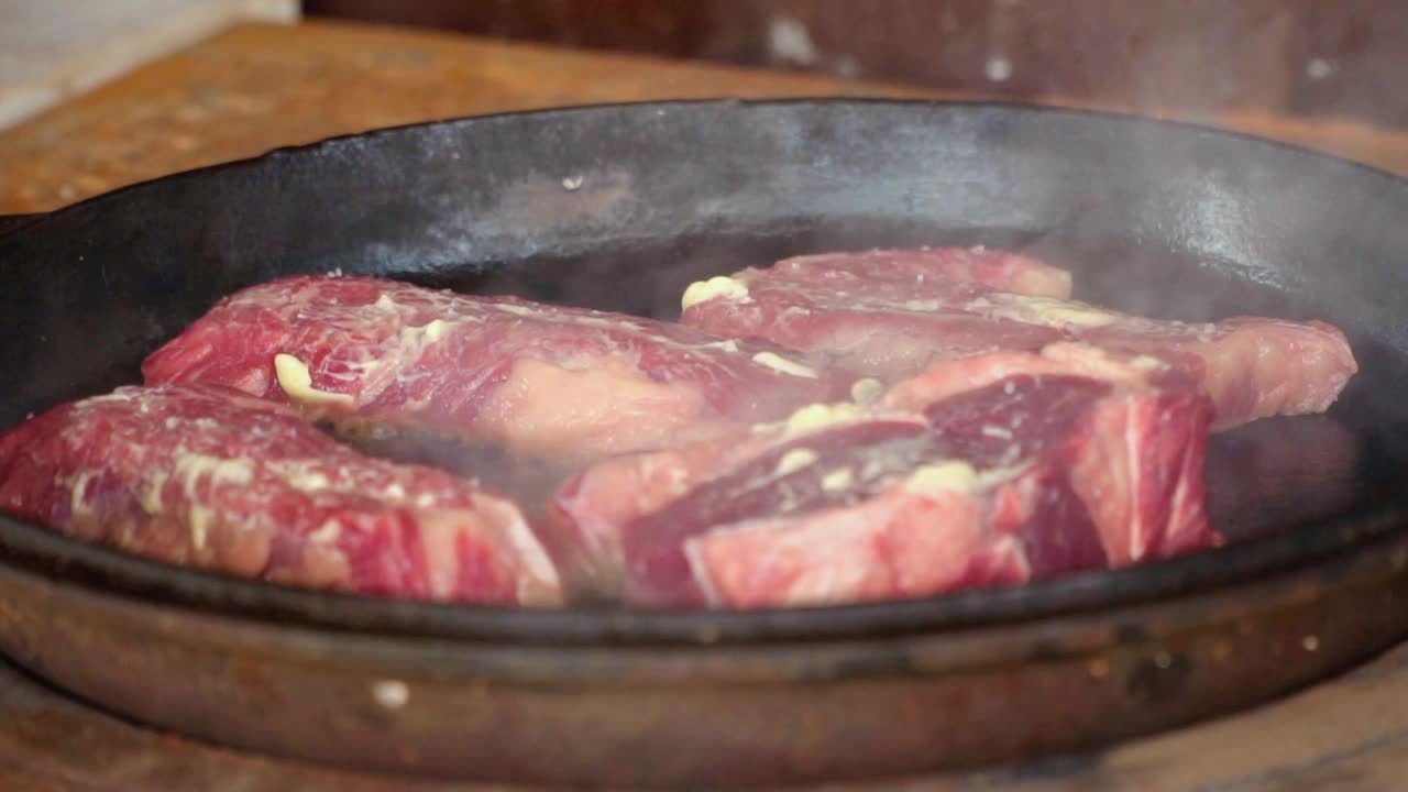 在铁锅里煎牛排。这家餐厅的专业厨师在家做饭。厨师把一块肉放在火上烤。煎烟。生肉蒸煮过程。