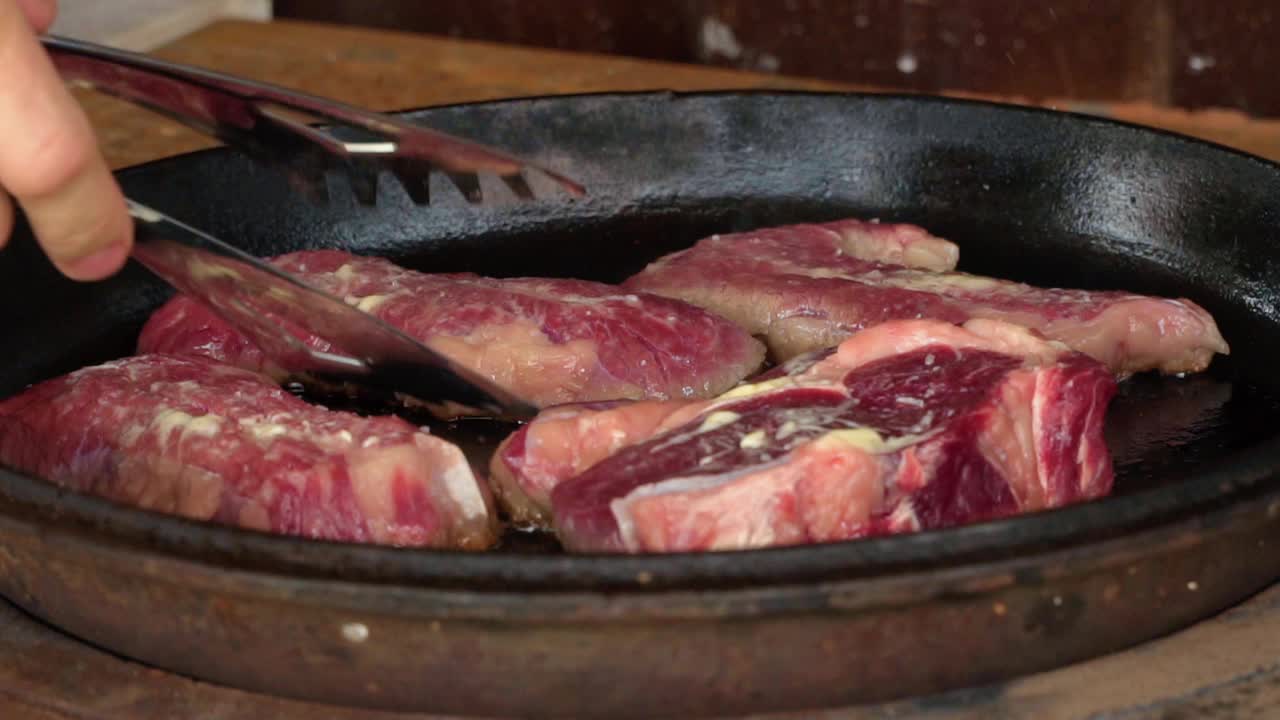 在铁锅里煎牛排。这家餐厅的专业厨师在家做饭。厨师把一块肉放在火上烤。煎烟。生肉蒸煮过程。