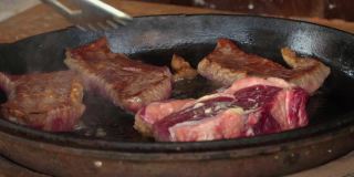 在铁锅里煎牛排。这家餐厅的专业厨师在家做饭。厨师把一块肉放在火上烤。煎烟。生肉蒸煮过程。
