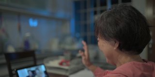 一名亚洲华裔老妇人晚上在厨房用数字平板电脑与她的儿子和儿媳进行视频通话