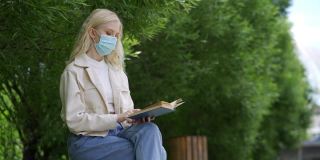 一名戴着医用口罩的学生在公园里看书。在冠状病毒流行期间进行户外学习。