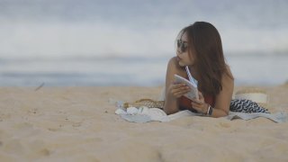 开朗的年轻女子在普吉岛海边的海滩上读书视频素材模板下载