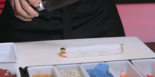厨师的手拿着刀，把它泡在水里切寿司卷