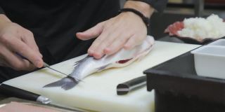 厨师熟练地用鱼刀将鲈鱼切开去骨