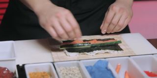 厨师的手在餐具垫上卷寿司，把寿司卷里外包起来