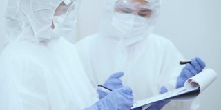 冠状病毒大流行期间，两名身穿防护服的医护人员在写字板上讨论血液检测结果。