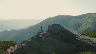 一个徒步旅行者站在一块岩石上，在日落时展望未来。运动员站在山顶眺望远方。从后面鸟瞰一个圆圈视频素材模板下载