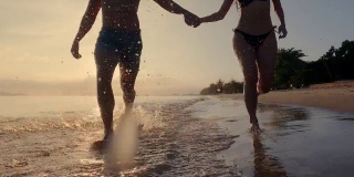 年轻的亚洲情侣在沙滩上散步和跑步。日落剪影橙光看起来很美。