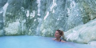 慢镜头:在意大利托斯卡纳的地热池和温泉中，一名成熟的女子正在洗澡。巴格尼圣菲利波天然热瀑布在早上没有人。森林中的白鲸。