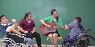 轮椅上的残疾少年在音乐课上教老师弹吉他，包括患有唐氏综合症的少女。亚洲美女老师学习有感觉幸福，积极的情绪。