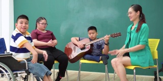 残疾少年与残疾少女用吉他演奏音乐，轮椅上的残疾学童团体，亚洲美女用快乐、积极的情绪拍手鼓励。