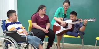 亚洲美丽的女教师教如何弹吉他，使学校的孩子感到幸福，积极的情绪，包括青少年唐氏综合症的女孩