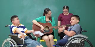 患有唐氏综合症的少女等待与她共舞的时间亚洲美女弹吉他鼓励，跳舞，唱歌与残疾学校儿童团体在轮椅上音乐会议课感受幸福，积极的情绪。