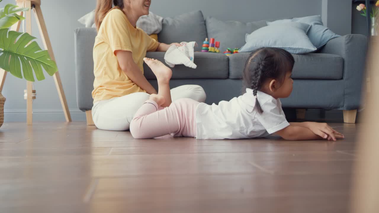 快乐快乐的亚洲家庭妈妈追逐着她可爱的烦躁的孩子，她在地板上爬行，在家里的客厅里玩耍放松。
