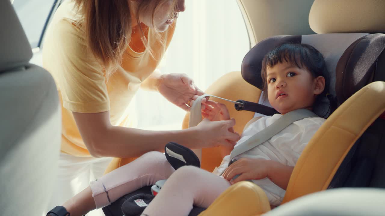 快乐快乐的亚洲家庭妈妈和蹒跚学步的女孩在车里准备出行前系好儿童汽车座椅安全带。