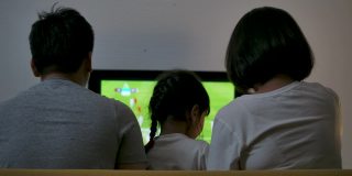 亚洲家庭坐在沙发上，一起看电视足球赛，为胜利和胜利而欢欣鼓舞。