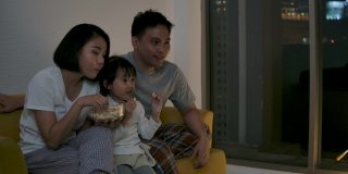 亚洲家庭坐在沙发上，一起看电视足球赛，为胜利和胜利而欢欣鼓舞。