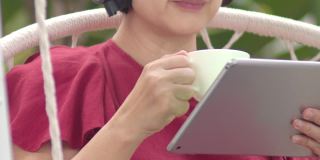 一名中年妇女在秋千上悠闲地听着平板电脑上的音乐