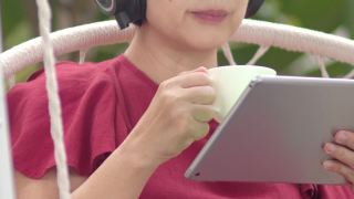 一名中年妇女在秋千上悠闲地听着平板电脑上的音乐视频素材模板下载