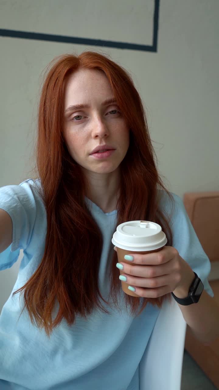 POV手持拍摄疲惫的年轻女子通过手机在线视频通话，喝咖啡从杯子看着相机。