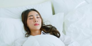 亚洲美丽舒适的女孩穿着睡衣躺在卧室的床上。有魅力的年轻女子开心的抱着舒适的枕头和毯子然后伸展，享受清晨醒来后在家里的房间里。