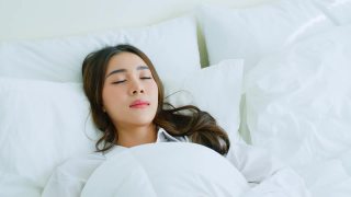 亚洲美丽舒适的女孩穿着睡衣躺在卧室的床上。有魅力的年轻女子开心的抱着舒适的枕头和毯子然后伸展，享受清晨醒来后在家里的房间里。视频素材模板下载