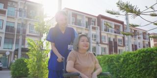 亚洲快乐的老病人奶奶在绿色公园户外玩。护理员微笑着推着坐在轮椅上举起手臂的老人，享受着养老院的炉边护理活动。